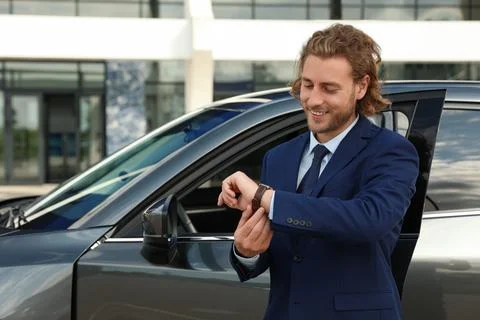 Attractive young man checking time near luxury car outdoors Stock Photos
