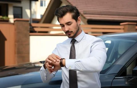 Attractive young man checking time near luxury car outdoors Stock Photos
