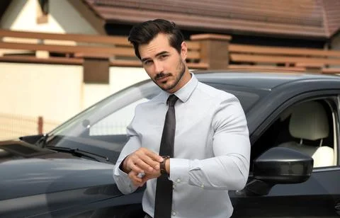 Attractive young man checking time near luxury car outdoors Stock Photos