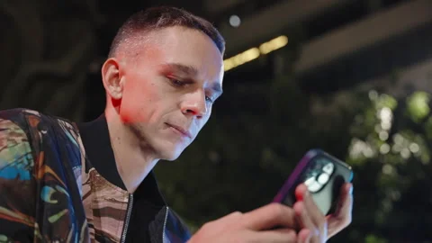 An attractive young man in a cool jacket at night writing a message on a phone Stock Footage 252849340