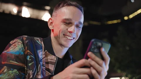 An attractive young man in a cool jacket at night writing a message on a phone Stock Footage 252849388