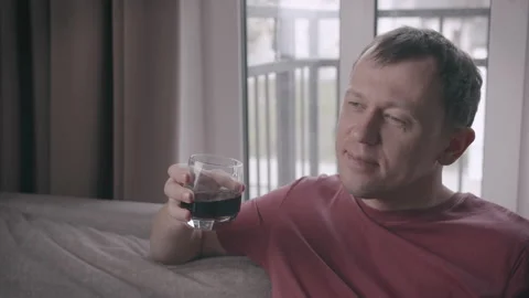 Attractive young man dreaming while sitting on sofa with glass of drink 스톡 동영상 158395151