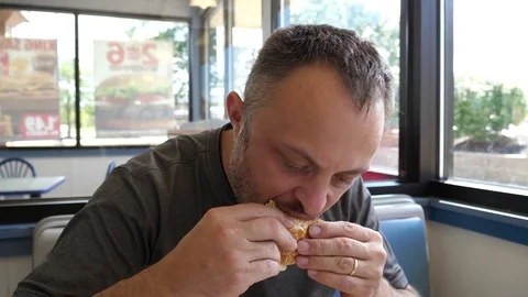 Attractive young man eats hamburger burger sandwich at the fast food restaurant Stock Footage 80746790