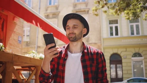 Attractive young man in the hat uses phone walk in city smile feel happy blurred Video stock 92070291