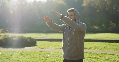 Attractive young man in a hood with the beard exercising in green park. Sunny Stock Footage 82499112