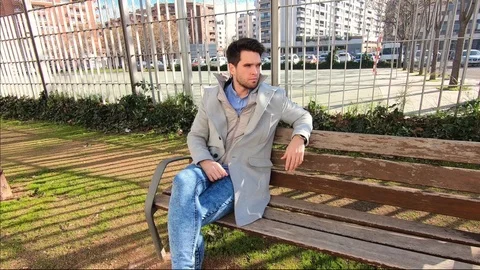 Attractive young man with jacket is sitting on a park side in winter. Видео 124197133
