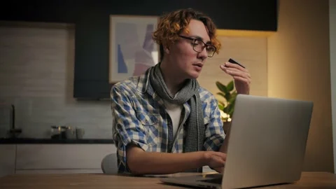 Attractive young man making online payment, holding bank card and using laptop Stock Footage 221619297