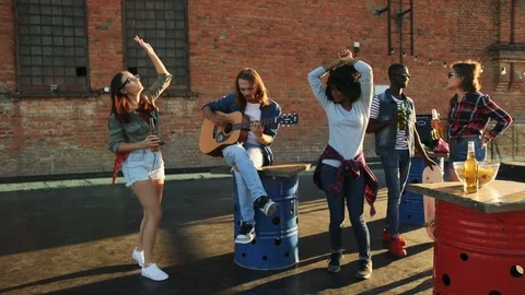 Attractive young man playing on the guitar among his dancing and chatting Stock Footage 81802430