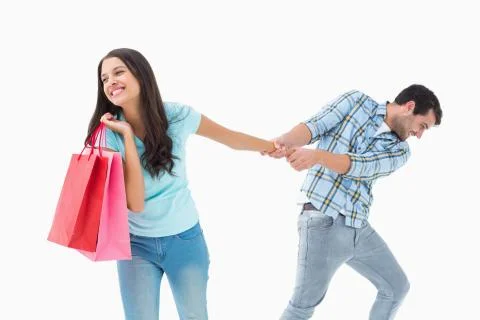Attractive young man pulling his shopaholic girlfriend Stock Photos