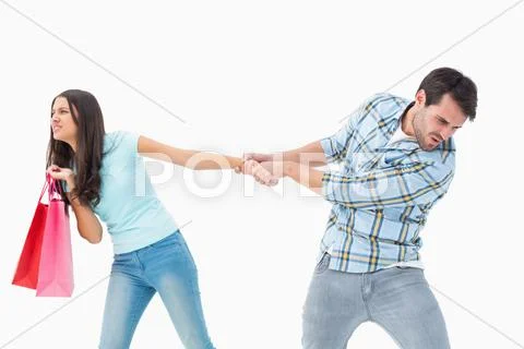 Attractive young man pulling his shopaholic girlfriend Stock Photos
