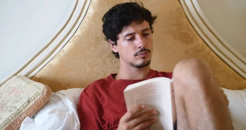 Attractive young man reading book in luxury bed Stock Footage 101741289