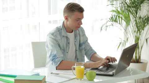 Attractive young man sitting at table using laptop and drinkig juice Stock Footage 27692035