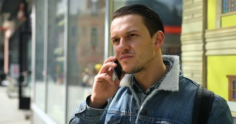 Attractive young man speaks on the phone in the city center on a sunny day Stock Footage