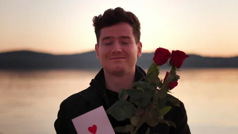 Attractive young man in stylish coat holds out bouquet of red roses and Love 库存影片 229661746