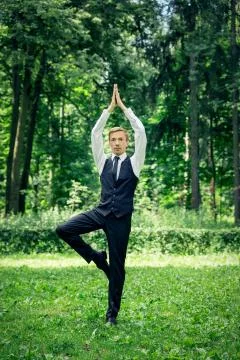 Attractive young man in a suit does yoga (tree pose) in a park. Stock Photos