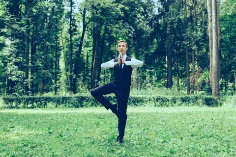 Attractive young man in a suit does yoga (tree pose) in a park. Stock Photos