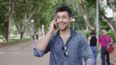 Attractive young man talks on his cell phone as he walks in a park Stock Footage 86836758
