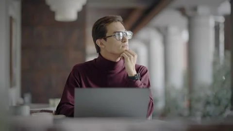 Attractive young man thinking while sitting at laptop in cafe in afternoon 스톡 동영상 343514054