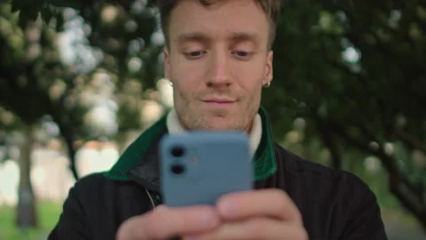 Attractive young man uses smartphone at the park at sunny day Stock Footage 150727162