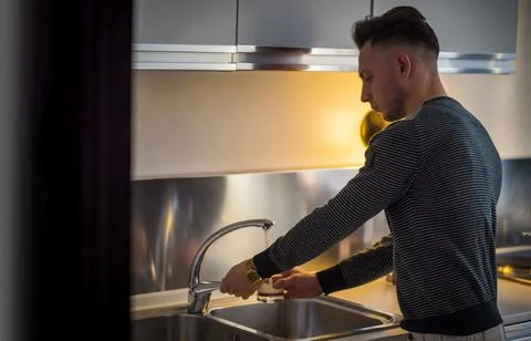 Attractive young man using tap water from kitchen sink Stock Photos