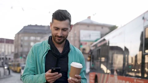 Attractive Young Man Walking Down the Street in Big Town. Holding Tasty Coffee Vídeo Stock 92426773