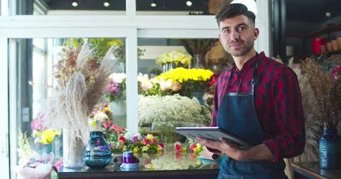 Attractive young man working in modern flower store using gadget. Handsome Stock Footage 138748890