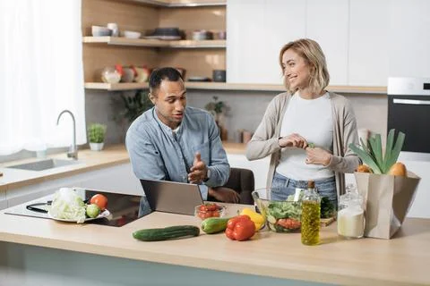 Attractive young multiethnic couple using laptop computer while preparing Stock Photos