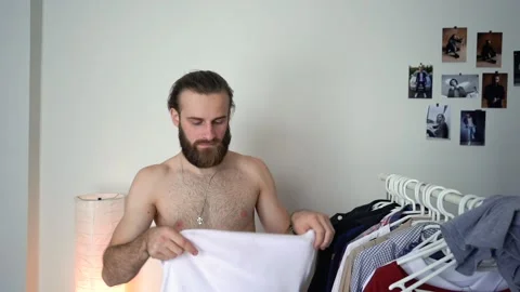 Attractive Young Stylish man is throwing a jacket on a mirror choosing a t-shirt Stock Footage 147900681