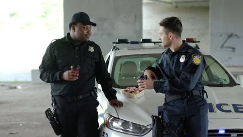 Attractive young two policemen drinking coffee and eating donut with appetite Stock Footage 112956477