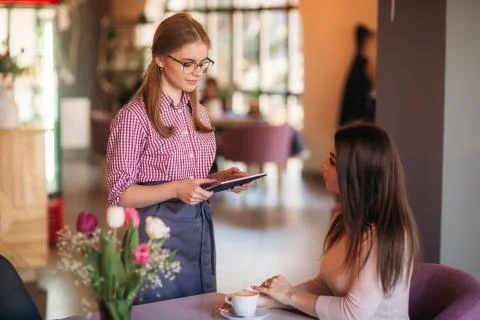 Attractive young waitress using a tablet computer to take an order from a Stock Photos