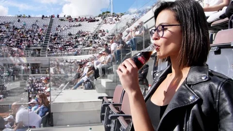 Attractive young woman drinking coca cola at the stadium  Stock Footage