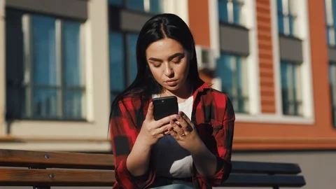 Attractive young woman in stylish red rock checkered shirt sitting on a bench Stock Footage 111220153