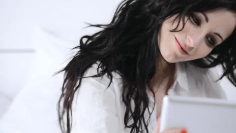 Attractive young woman using tablet computer touchscreen in her bedroom. Stockbeeldmateriaal 199628767