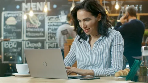 Attractive Young Woman Works on a Laptop Computer while Sitting in Cafe. Stock Footage