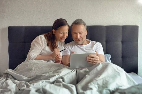 Attraktives Ehepaar sitzt im Bett und trinkt Kaffee Happy middle-aged coup... Stock Photos