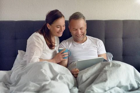 Attraktives Ehepaar sitzt im Bett und trinkt Kaffee Happy middle-aged coup... Stock Photos