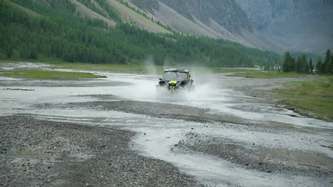 AtV buggy quickly rides along a mountain river throwing aside the spray Stock Footage