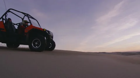 ATV four wheeler side by side drives across a sand dune at sunset Stock Footage 148304653