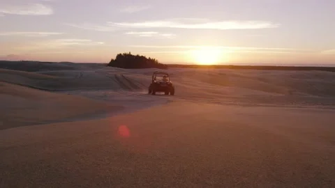 ATV four wheeler side by side drives across a sand dune at sunset Stock Footage 148304677