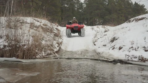 ATV jump scene. All terrain vehicle vaults over snow into freezing water Stock Footage 334783611
