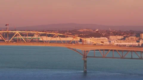 Auckland Harbour Bridge at sunset with container ships and cranes, NZ Stock Footage 337868991