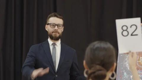 Auctioneer Pointing at Paddles and Calling Out Bids during Auction Stock Footage 124244071