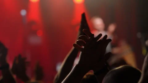 Audience clapping hands in excitement at a live music concert with vibrant red Stock Footage 313638565