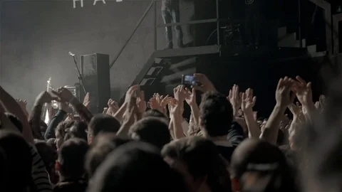 Audience with hands raised at a music festival and lights streaming down from Stock Footage