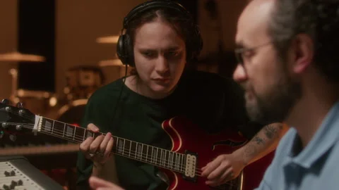 Audio Engineer Controlling Mixing Console as Music Artist Playing Guitar Stock Footage 334370979
