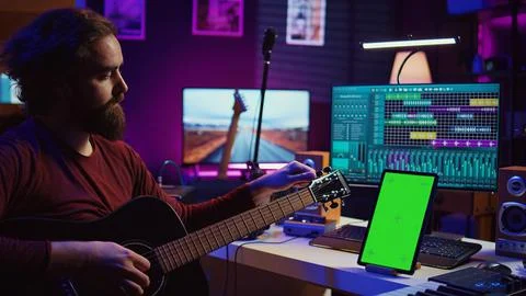 Audio engineer practices tuning his acoustic guitar in home studio Stockfoto's