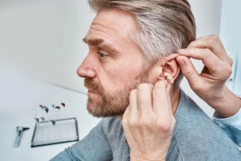 Audiologist inserting ITE hearing aid in adult man's ear at audiology cente.. Foto stock