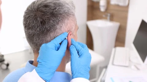 Audiologist installing hearing aid on ear of adult man in hearing clinic. Dea Stock Footage 316953237