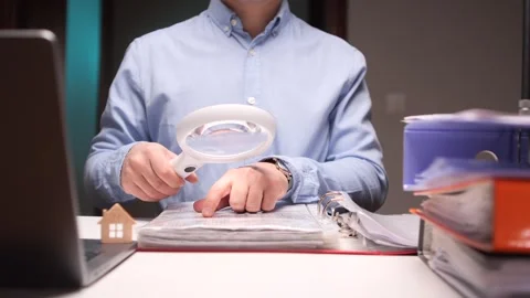 Auditor using magnifying glass analyzing financial documents at office desk Stock Footage 306267275