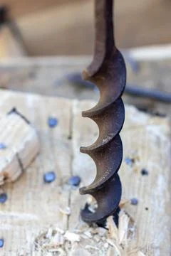 Auger drill bit embedded in wood with shavings in carpentry workspace Фото